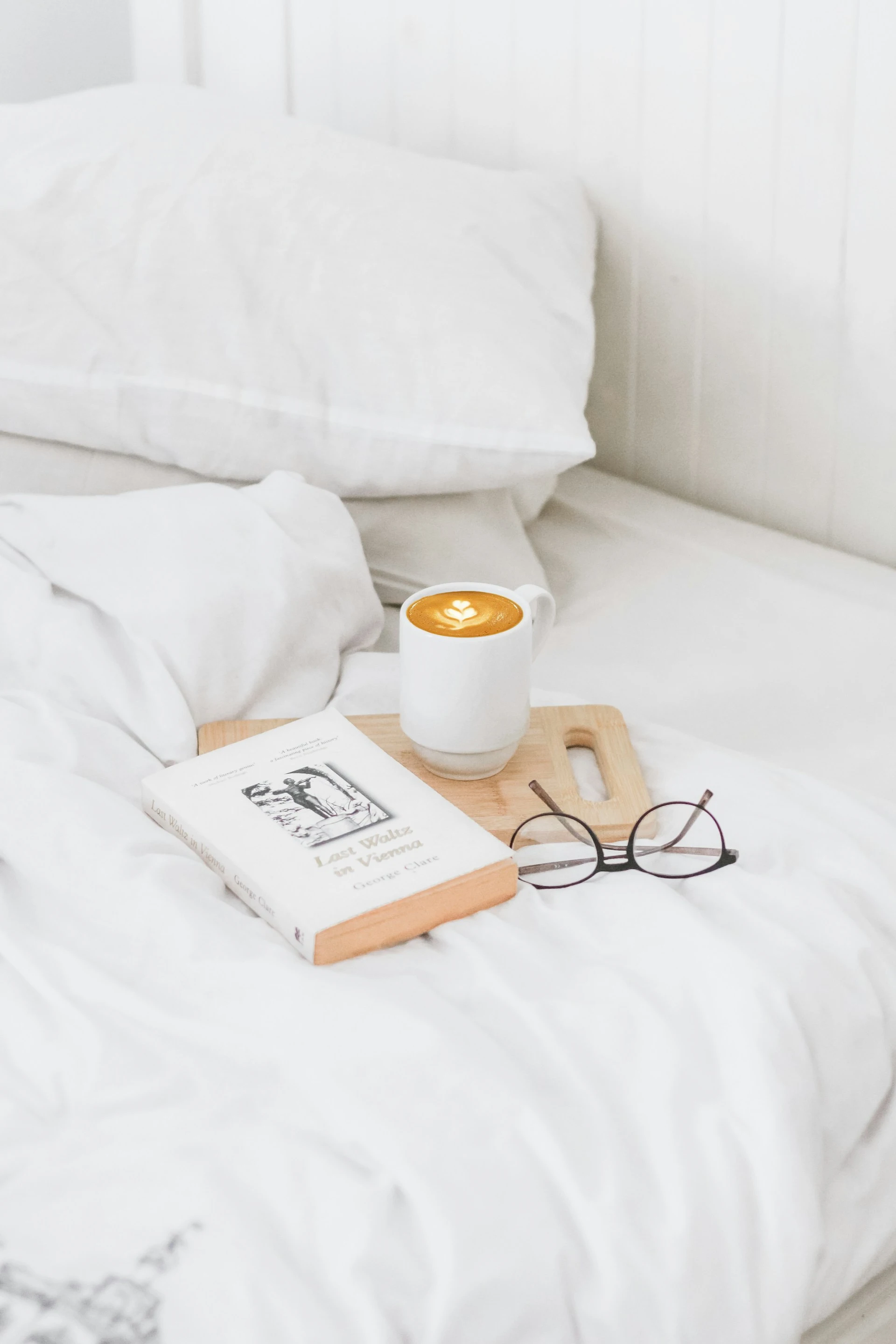 Чашка кави, книга і окуляри на ліжку